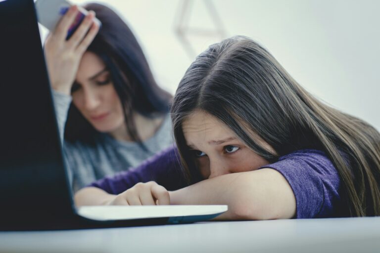 Jeune fille triste devant un ordinateur avec sa maman à côté