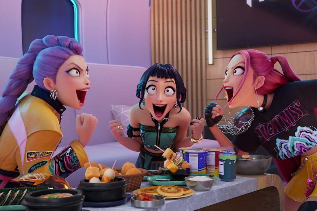 Image du film Kpop Demon Hunters où l'on voit les trois chanteuses faire des grimaces de joier au-dessus d'une table remplie de nourriture